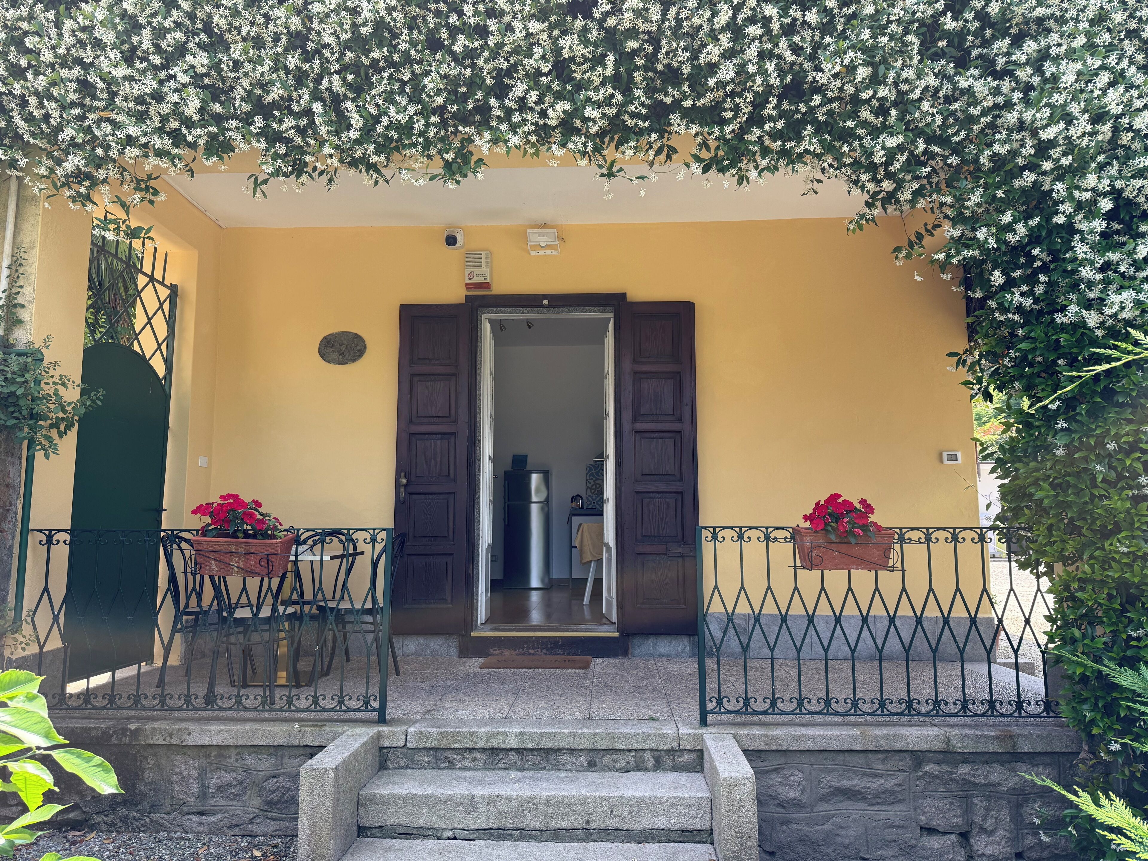 A yellow building with a wooden door, a stone staircase, and two potted plants.