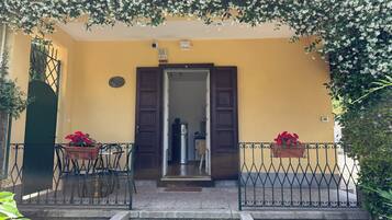 A yellow building with a wooden door, a stone staircase, and two potted plants.