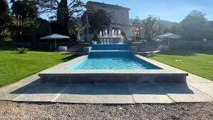Una piscina con una fuente, rodeada de un césped cuidado y un edificio al fondo.
