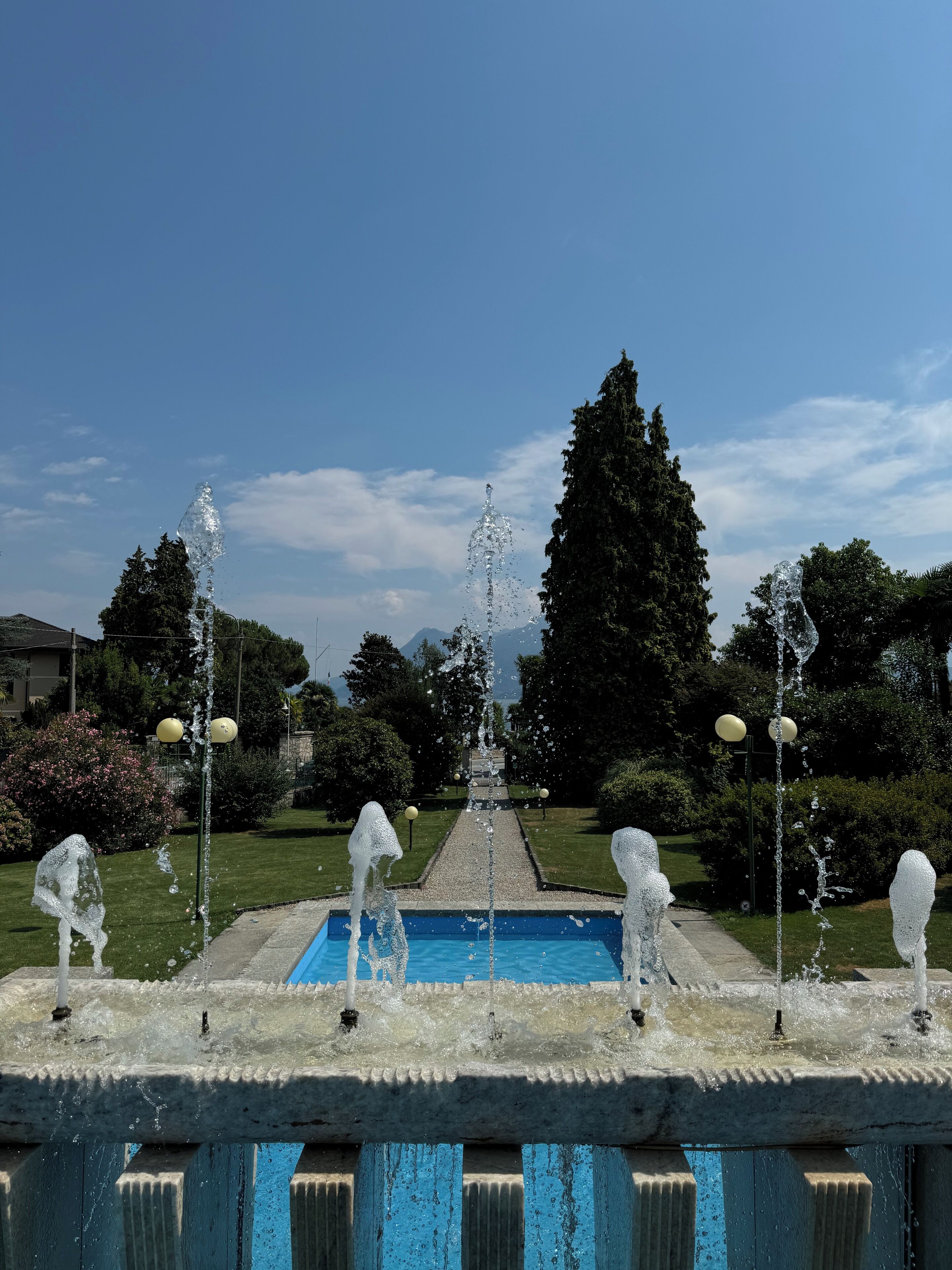 A fountain with multiple water jets, a central water feature, and a pool in the background.