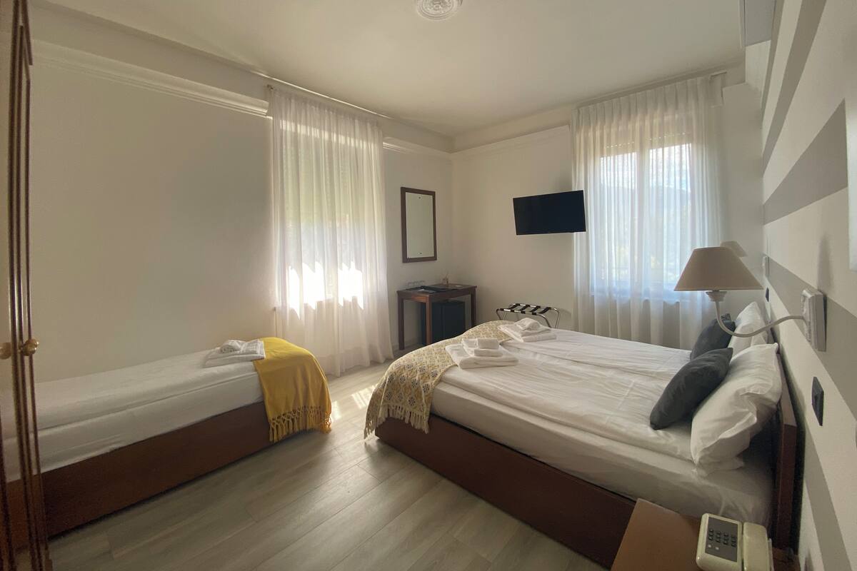Una camera d'albergo con due letti singoli, una TV montata a parete, un comodino con una lampada e un telefono.