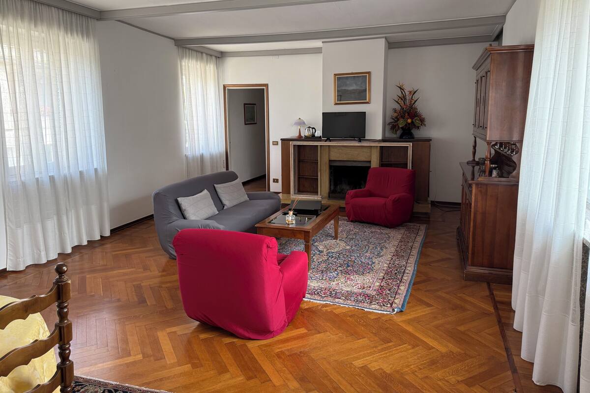 Un soggiorno con un divano grigio, una poltrona rossa, un tavolino da caffè, un camino e una televisione.