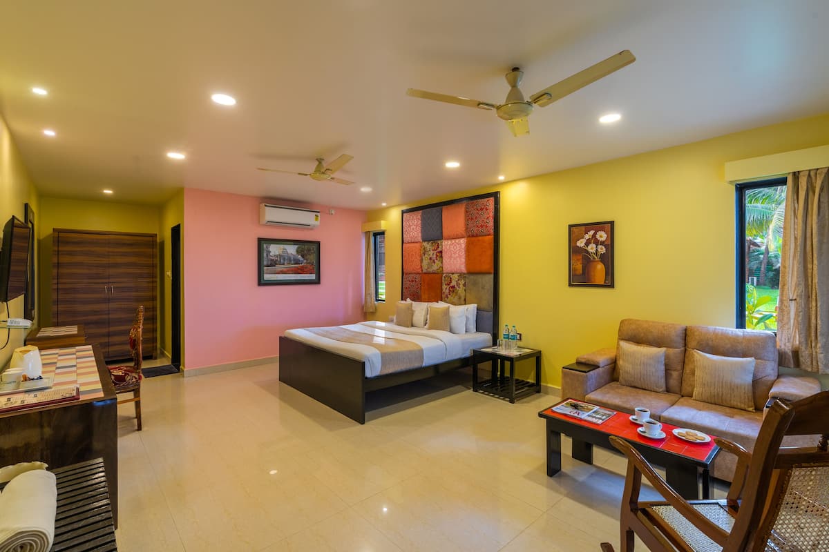 A hotel room with a bed, a sofa, a desk with a chair, a coffee table, and a ceiling fan.