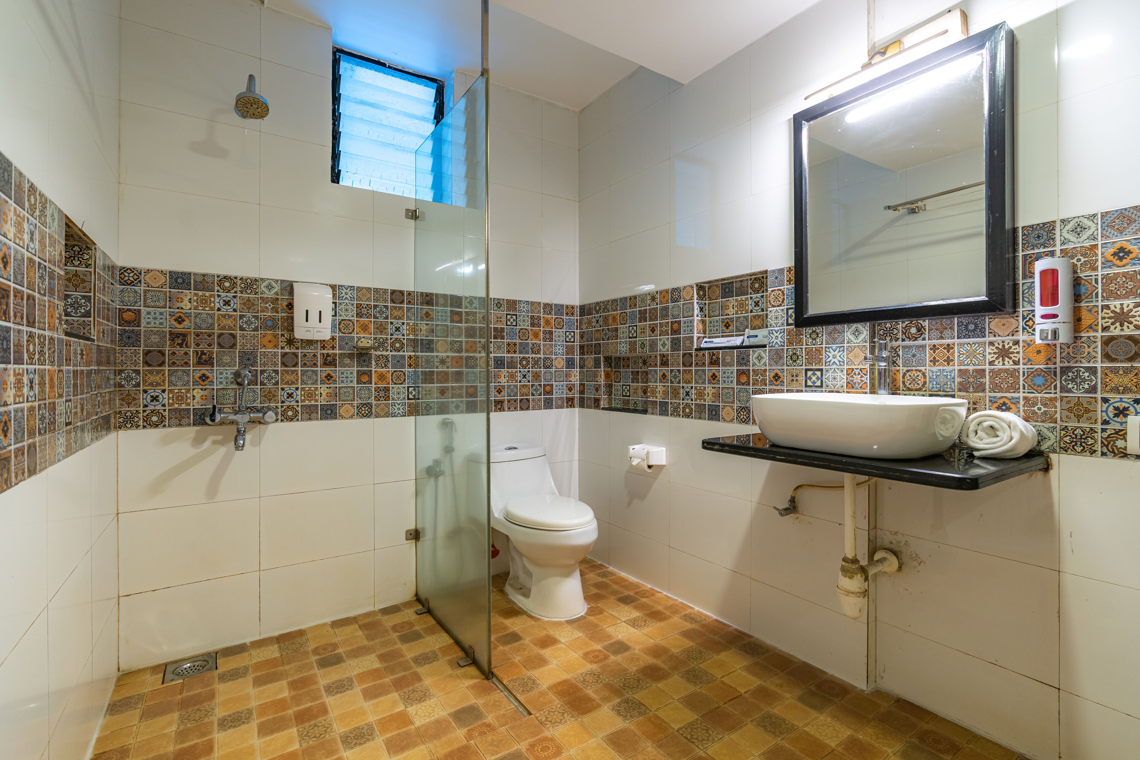 A bathroom with a tiled floor, a toilet, a sink with a mirror, and a shower.