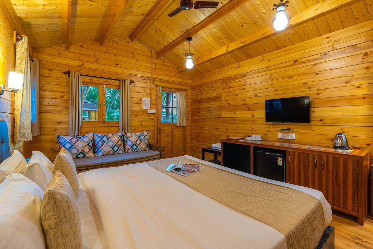 A wooden cabin room with a bed, a sofa, a television, and a small kitchenette.