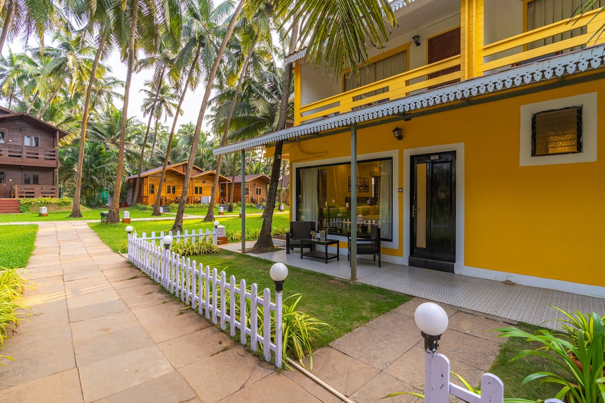 A yellow building with a balcony, a white fence, and a pathway leading to the entrance.