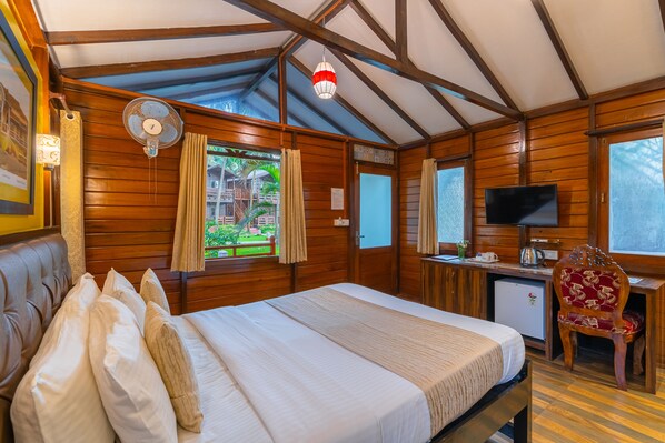 A wooden cabin room with a bed, a desk, a television, and a window with curtains. - La Cabana Beach and Spa (Ashvem)