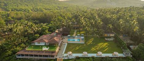 An aerial view of a resort with a swimming pool, multiple buildings, and lush greenery.