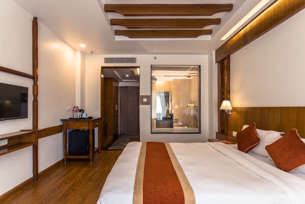 A hotel room with a large bed, wooden headboard, a flat-screen TV, a desk with a chair, and a mirror. - Landmark Pokhara (Pokhara)