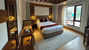 Habitación de hotel moderna con una cama grande, un escritorio, una silla y vistas de la ciudad a través de amplias ventanas.