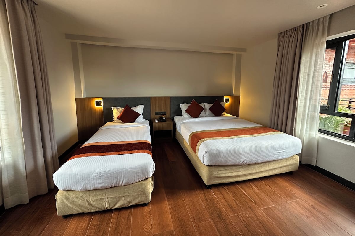 Une chambre d’hôtel avec deux lits, un plancher en bois et une fenêtre donnant sur un immeuble en briques.