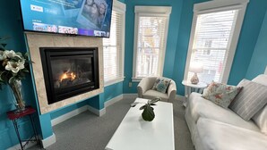 A living room with a fireplace, a flat-screen TV mounted above it, and a sofa. - Lotus Provincetown (Provincetown)