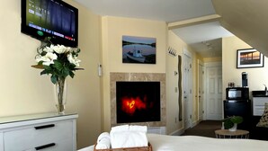 A hotel room with a bed, a TV mounted on the wall, a fireplace, a painting, and a kitchenette. - Lotus Provincetown (Provincetown)