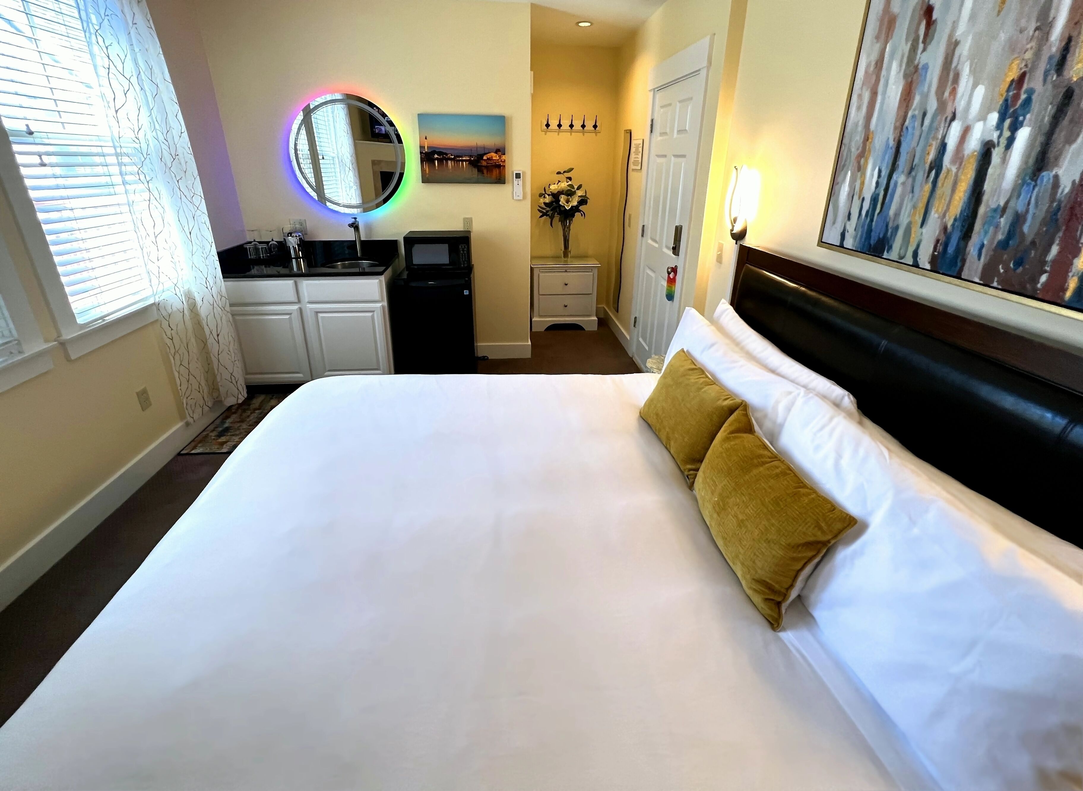 Habitación de hotel con una cama grande, un espejo redondo, un cuadro, un escritorio pequeño y un microondas.