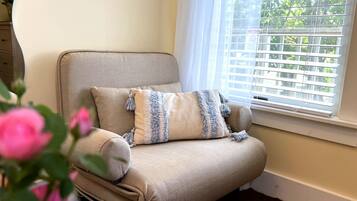 A beige armchair with a striped throw pillow and a window with blinds.