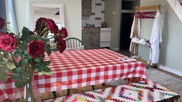 Un comedor con mantel a cuadros, un jarrón de rosas, un camino de mesa tejido y colorido, y una cocina al fondo.