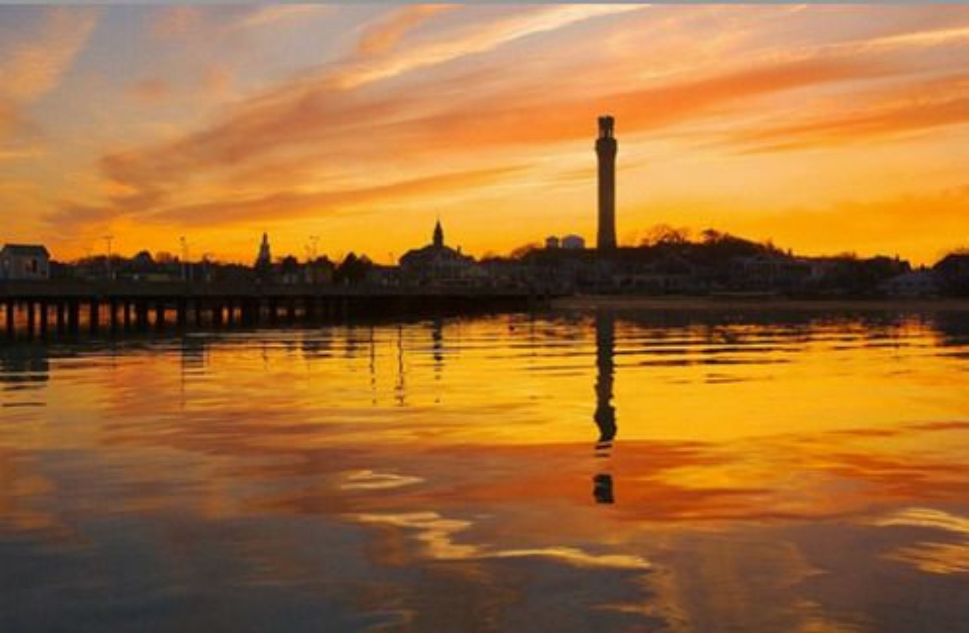 A sunset over a body of water with a prominent tower in the distance.