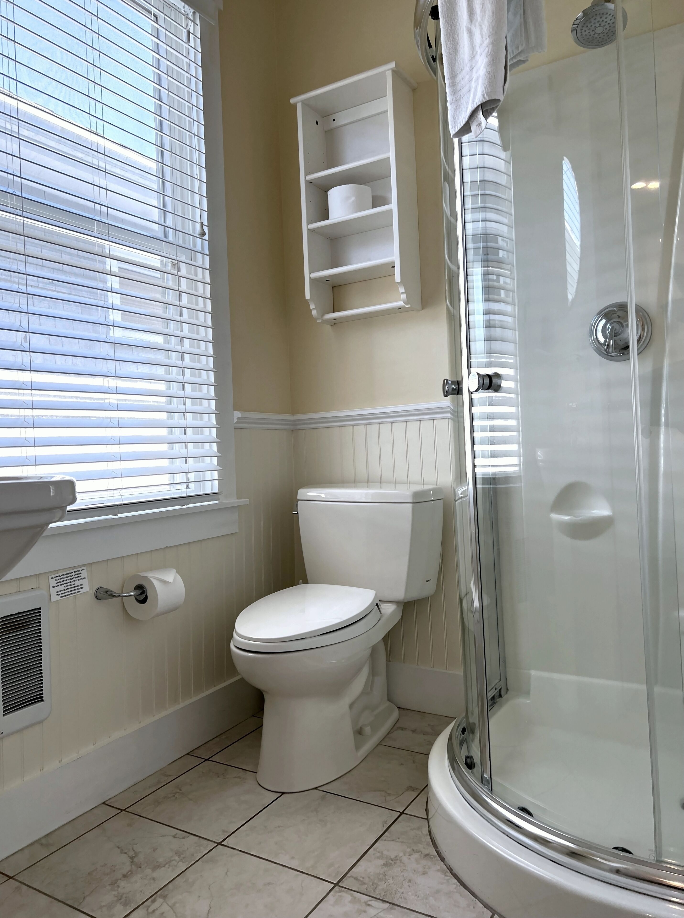 Un baño con inodoro, ducha y ventana con persianas.