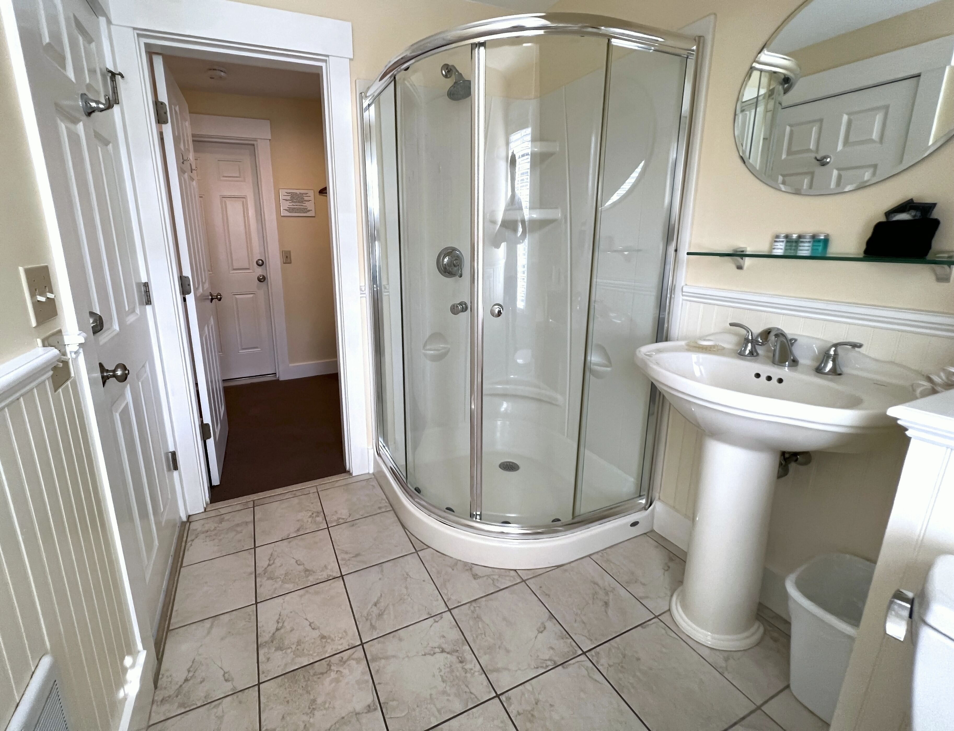 A bathroom with a glass shower enclosure, a pedestal sink, and a mirror above the sink.