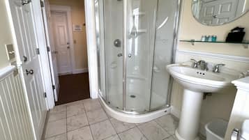 A bathroom with a glass shower enclosure, a pedestal sink, and a mirror above the sink.