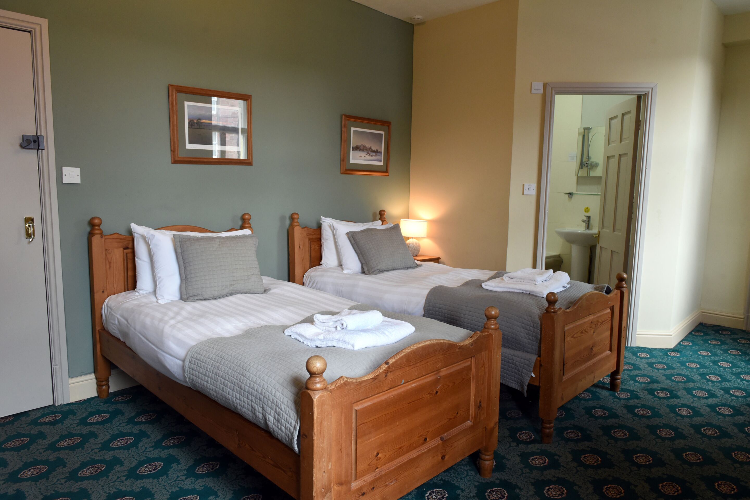 A hotel room with two wooden beds, a bathroom with a mirror, and a patterned carpet.