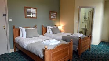 A hotel room with two wooden beds, a bathroom with a mirror, and a patterned carpet.