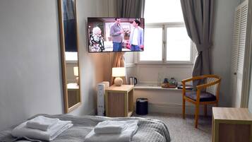 A hotel room with a bed, a television, a chair, a desk, and a window with curtains.