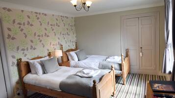 A hotel room with two wooden beds, a striped carpet, a floral wallpaper, and a white door.