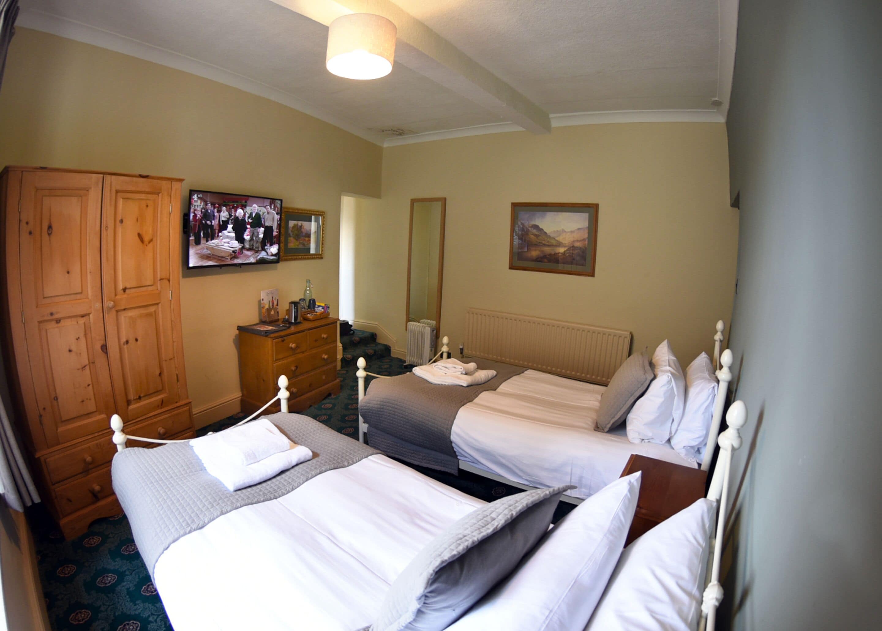 Una habitación de hotel con dos camas, un armario de madera, un televisor y un cuadro en la pared.