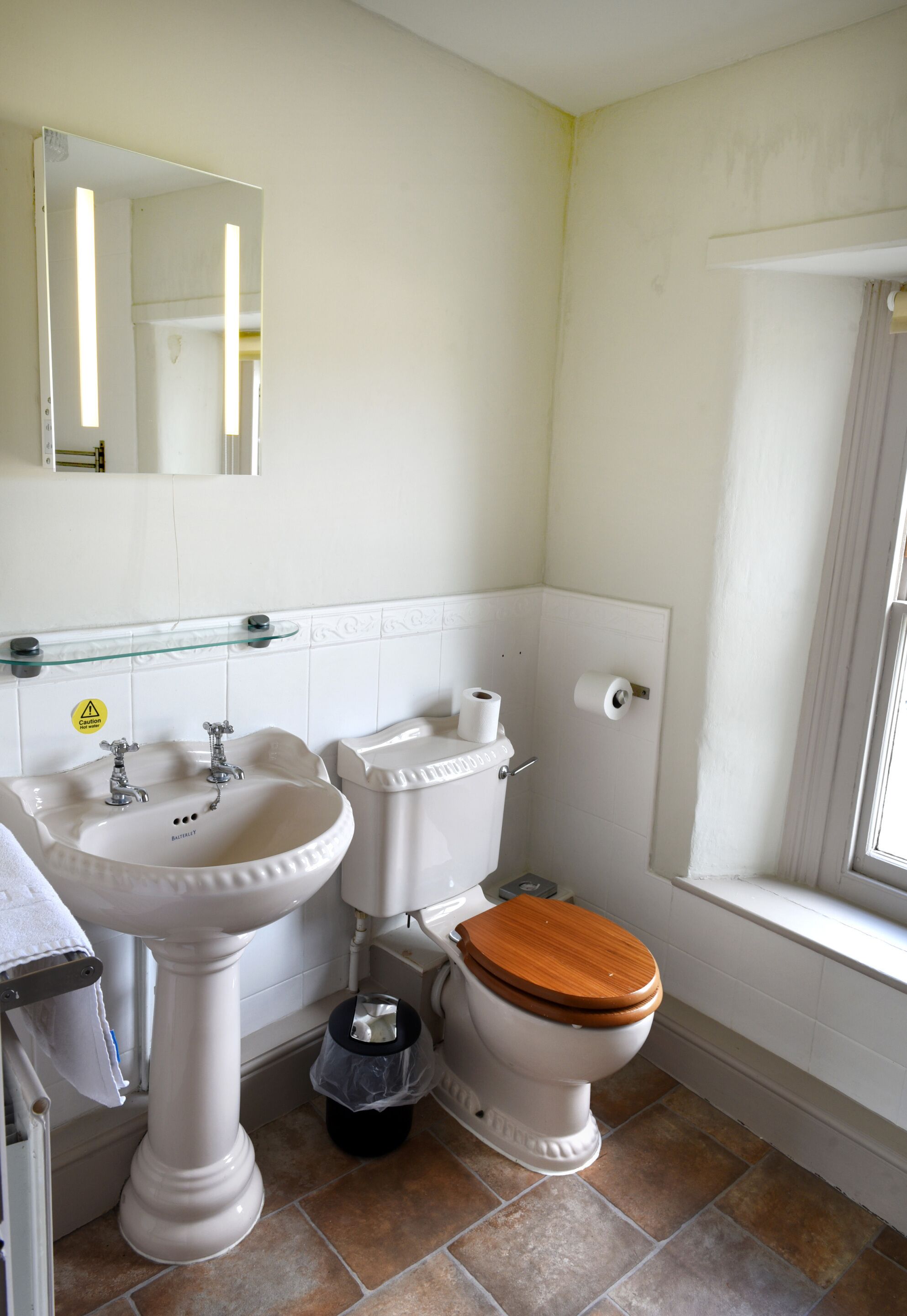 A bathroom with a pedestal sink, toilet, and a window with a curtain.