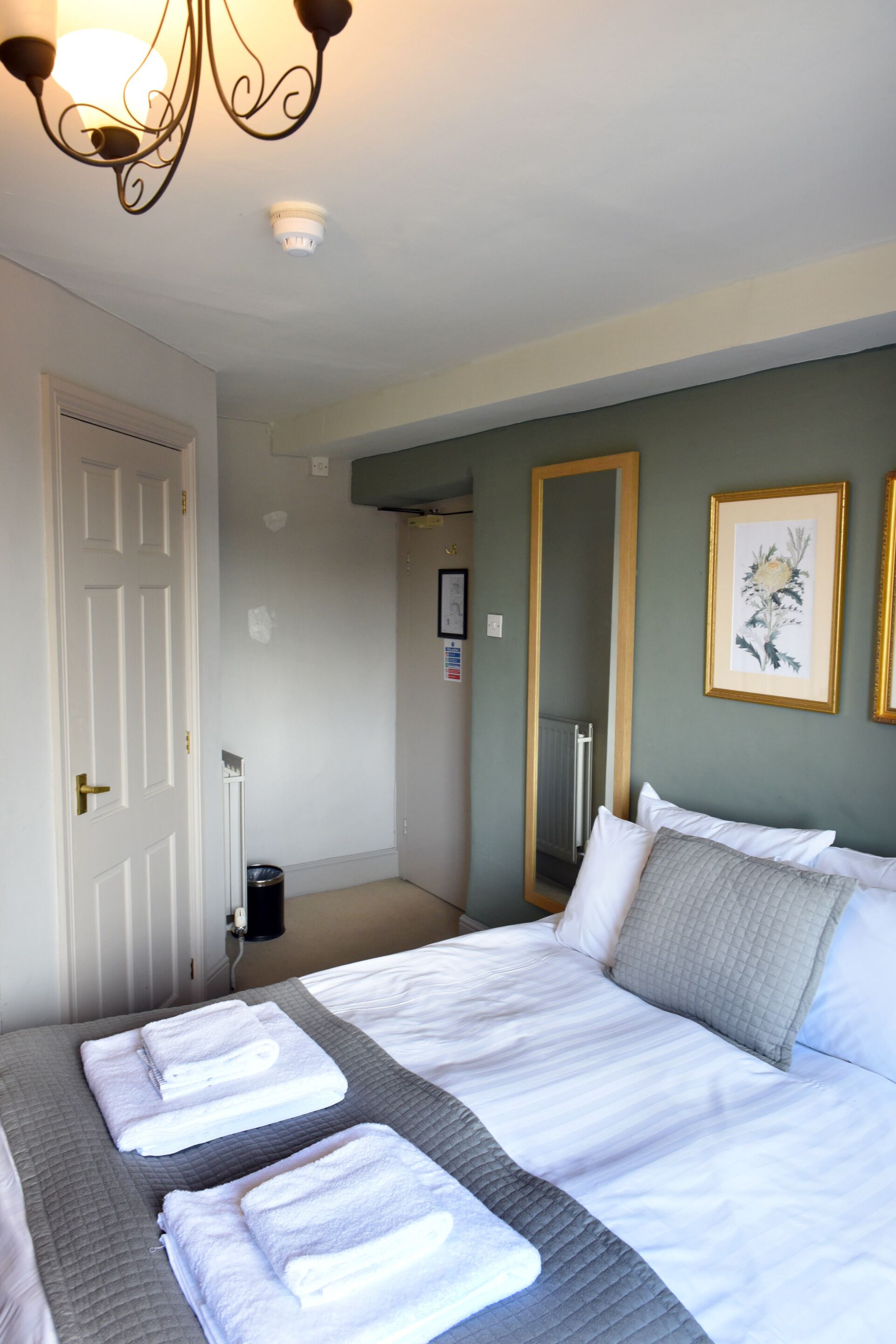 Une chambre d’hôtel avec un lit, une porte, un radiateur et un miroir.