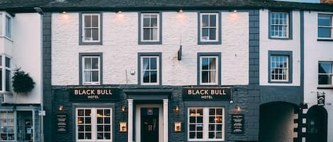 Un bâtiment à deux étages, orné d’enseignes indiquant « Black Bull Hotel », doté d’une façade en pierre et d’une entrée de style traditionnel.