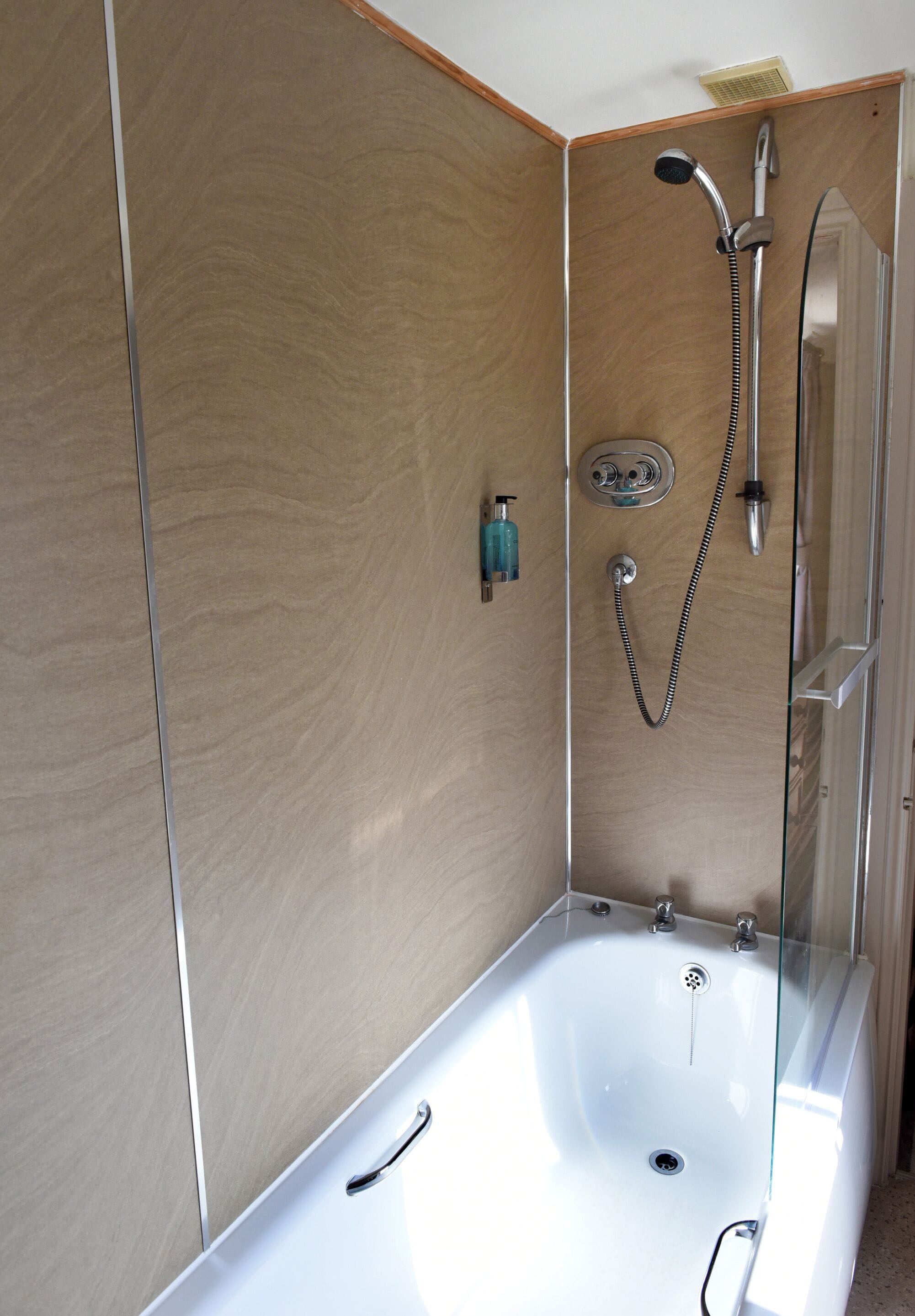 A modern bathroom with a glass-enclosed shower, a white bathtub, and a wooden wall.