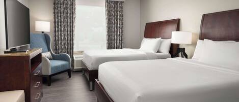 A hotel room with two beds, a TV, a desk, a chair, and a window with curtains.