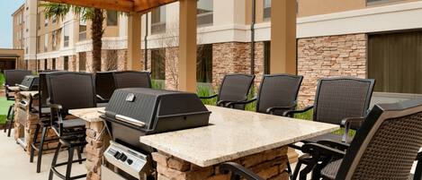 Un patio al aire libre con mobiliario de piedra y madera, una parrilla y vistas a un edificio de fachada de piedra.