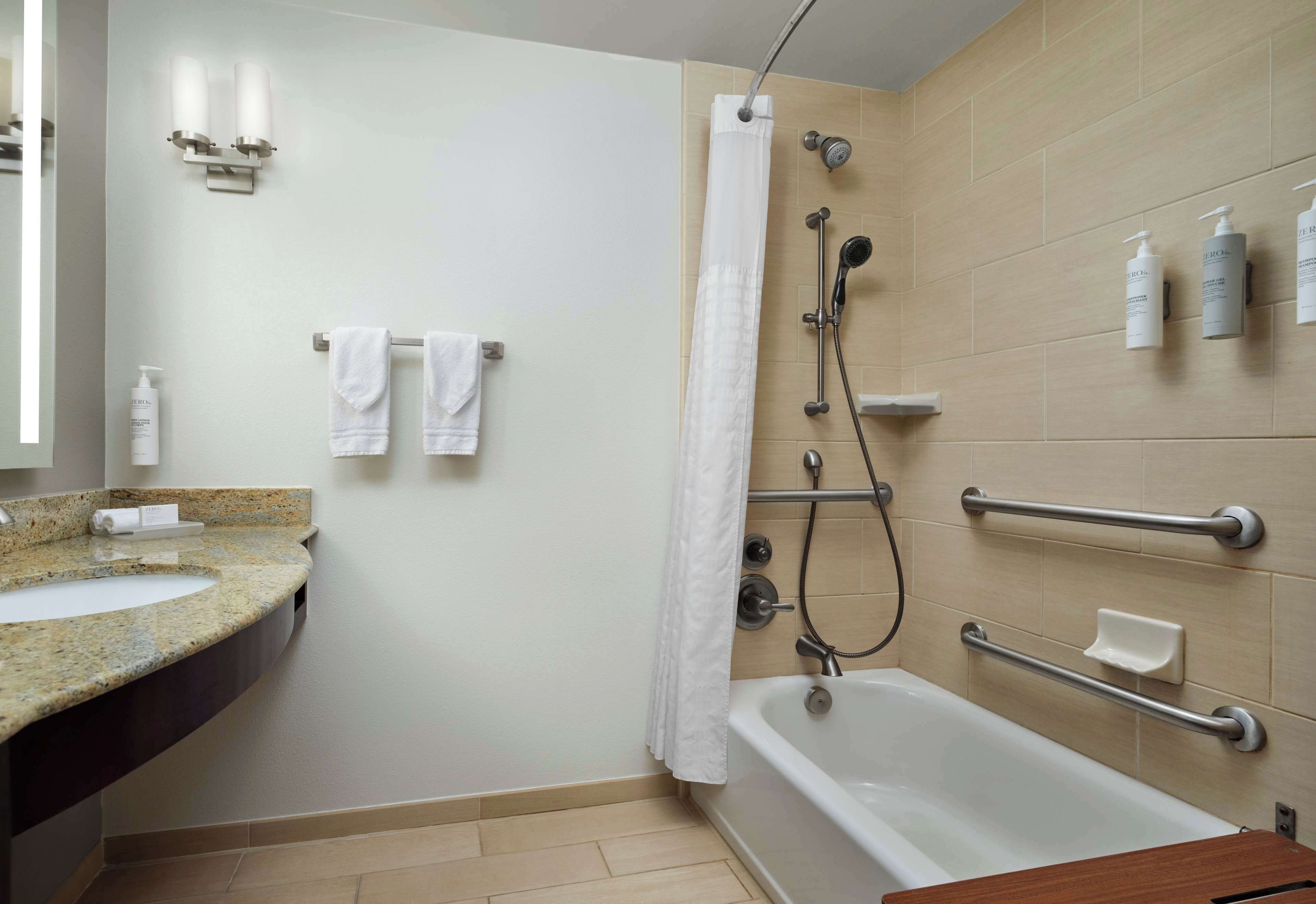 A modern bathroom with a bathtub, shower, and handrails.