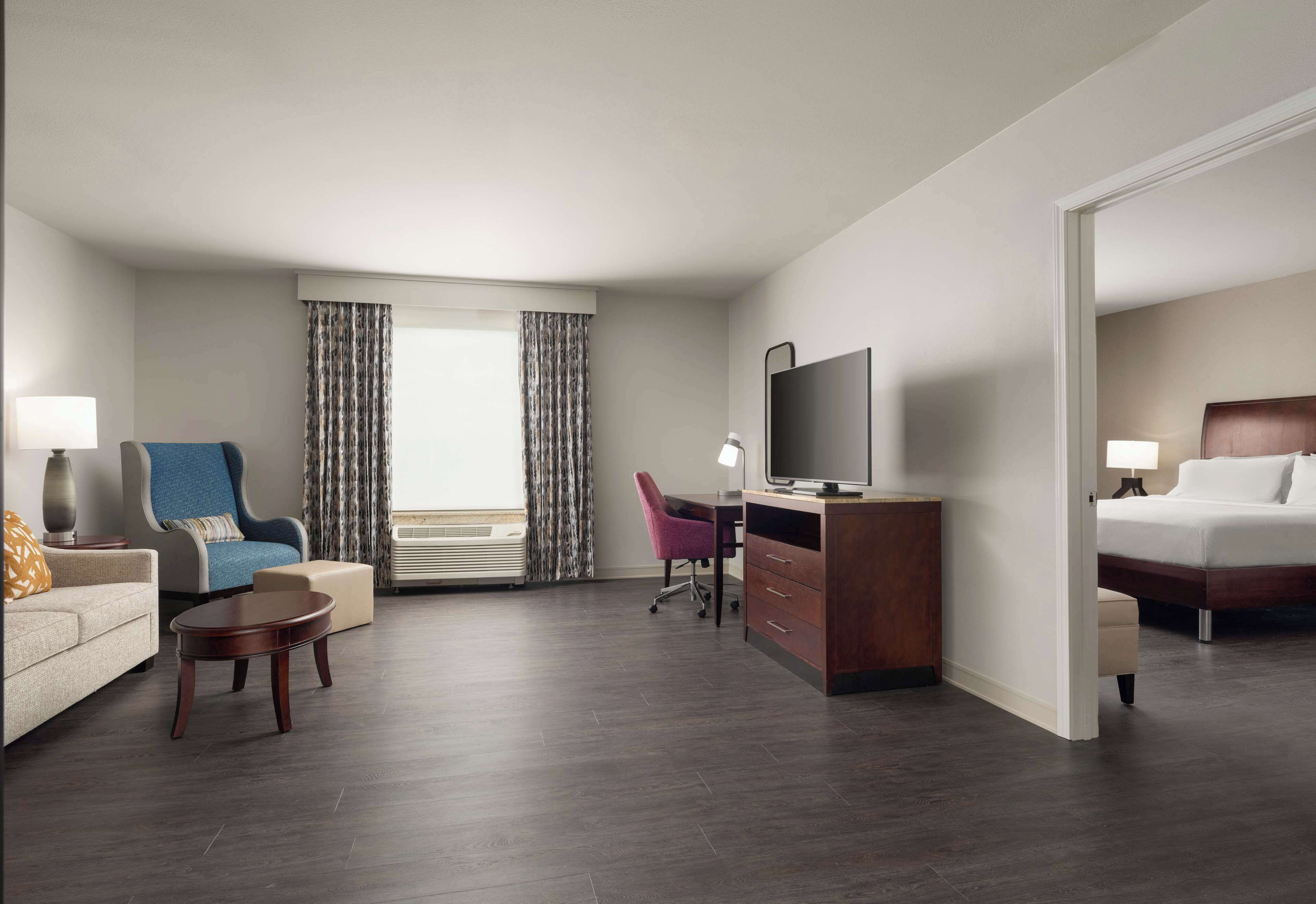 A hotel room with a sofa, armchair, desk, TV, and a bed.