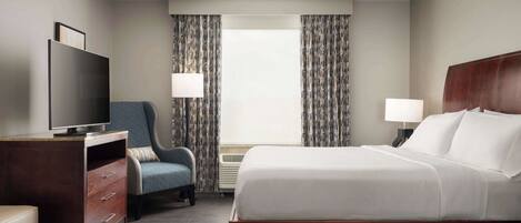 A hotel room with a bed, a TV, a desk, a chair, and a window with curtains.