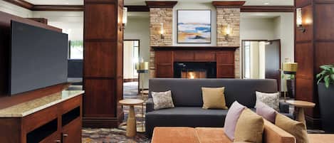 A spacious living area with a dark-colored sofa, multiple cushions, a fireplace, and a television on a wooden cabinet.