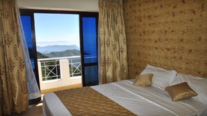 Een hotelkamer met een groot bed, uitzicht op bergen via een balkon, en behang met een patroon.