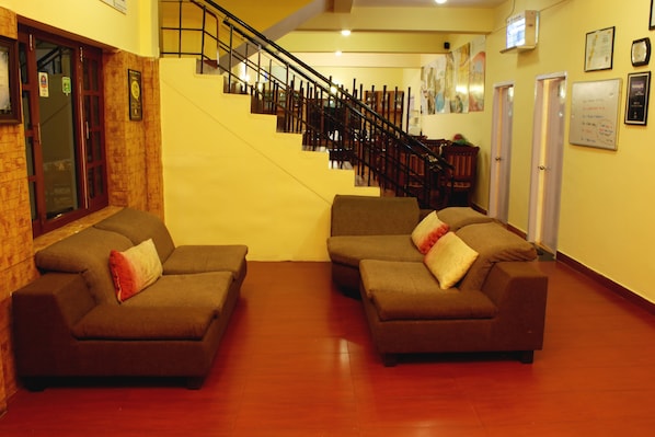 A hotel lobby with two sofas, a staircase, wooden flooring, and a reception desk. - Country Club Valley Vista (Kodaikanal)