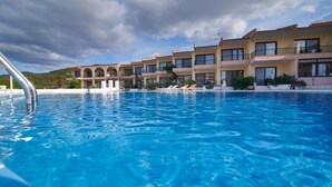 A swimming pool with clear blue water, surrounded by a row of multi-story buildings with balconies. - Toroni Blue Sea Hotel & Spa (Sithonia)