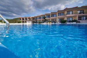 A swimming pool with clear blue water, surrounded by a row of multi-story buildings with balconies.