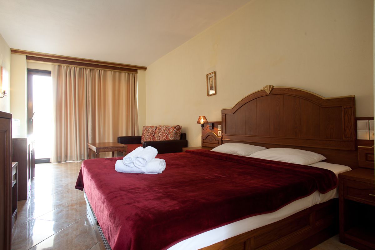 A hotel room with a large bed, a wooden headboard, a desk, and a chair.
