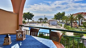 A balcony with a view of a pool and beach, featuring a table with chairs and lanterns. - Toroni Blue Sea Hotel & Spa (Sithonia)