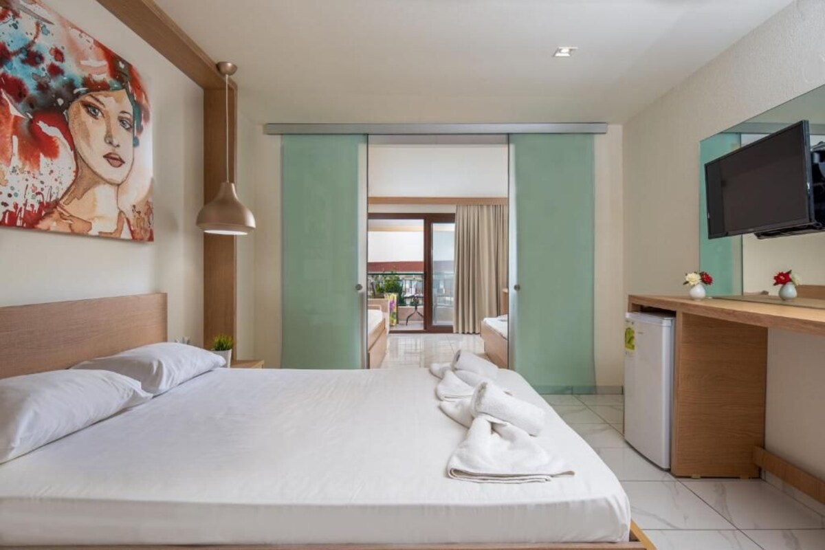 A hotel room with a bed, a desk, a television, and a painting on the wall.