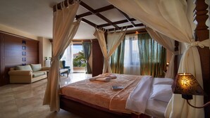 A bedroom with a bed, curtains, a nightstand, a lamp, and a view of the outside. - Toroni Blue Sea Hotel & Spa (Sithonia)