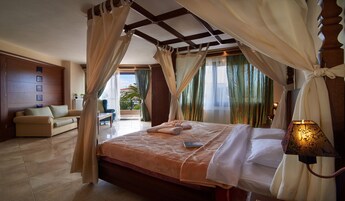 A bedroom with a bed, curtains, a nightstand, a lamp, and a view of the outside.