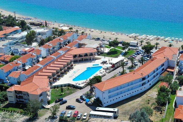 An aerial view of a coastal hotel with a swimming pool, beach access, and multiple buildings with red-tiled roofs. - Toroni Blue Sea Hotel & Spa (Sithonia)