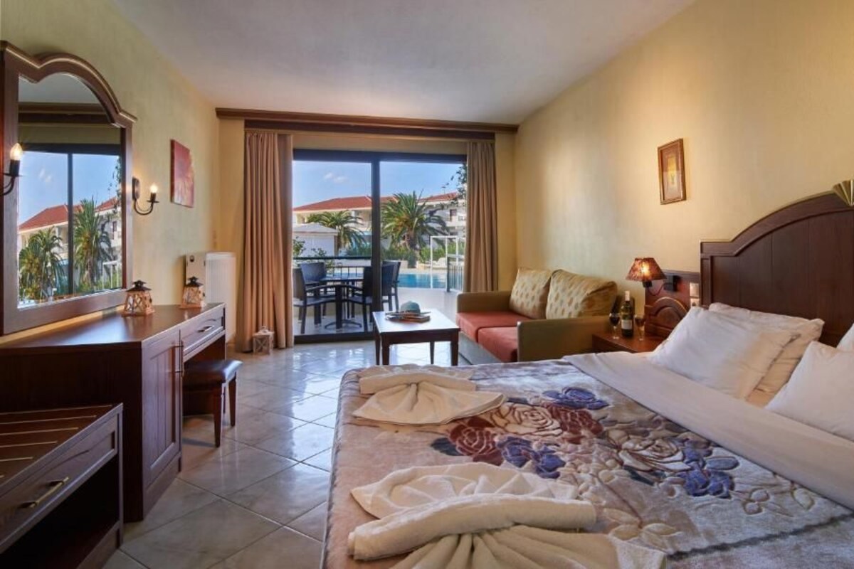 A hotel room with a large bed, a desk, a chair, and a view of the pool and palm trees.